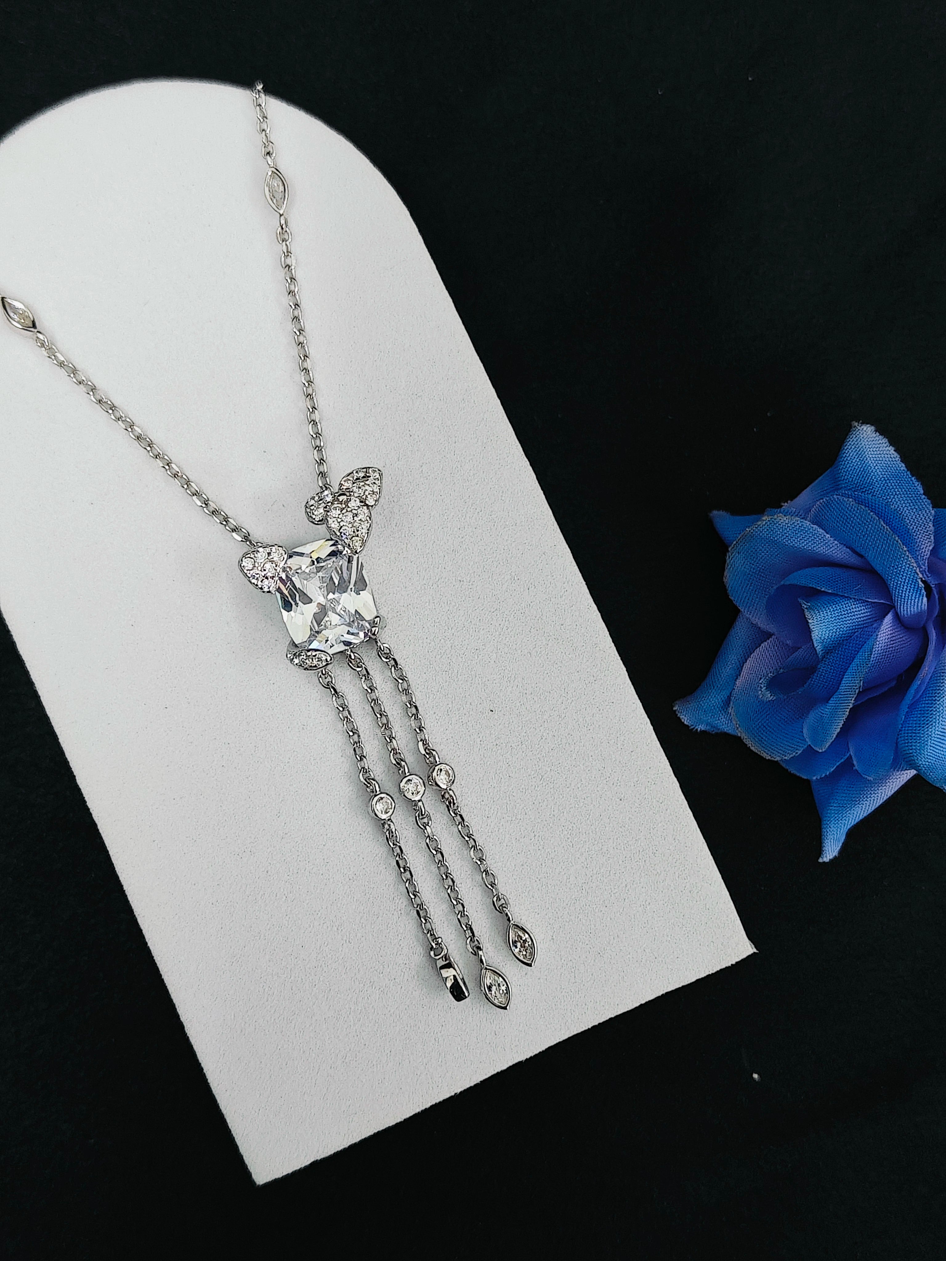 Silver necklace with a heart-shaped pendant on a white card with a blue rose in the background